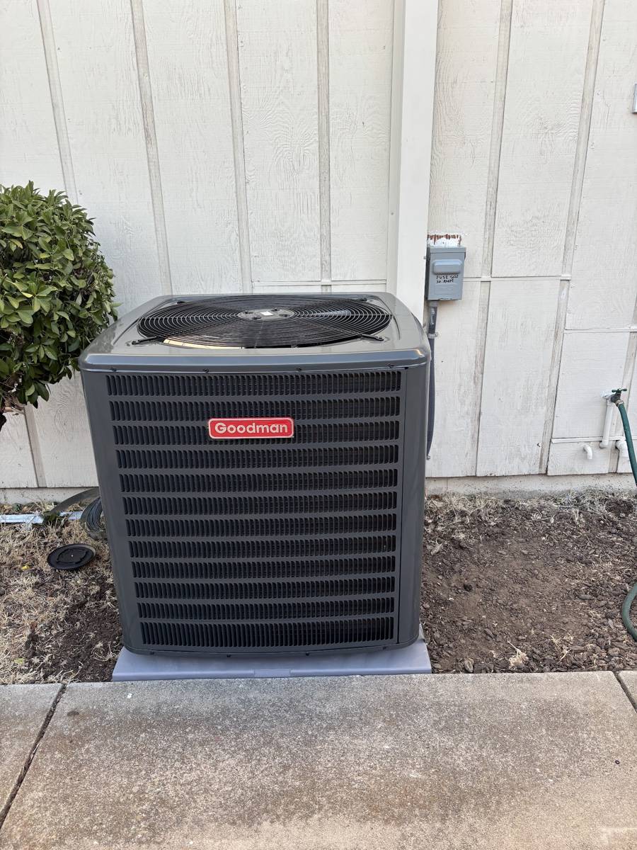 A new Goodman condenser on a fresh concrete pad beside a house