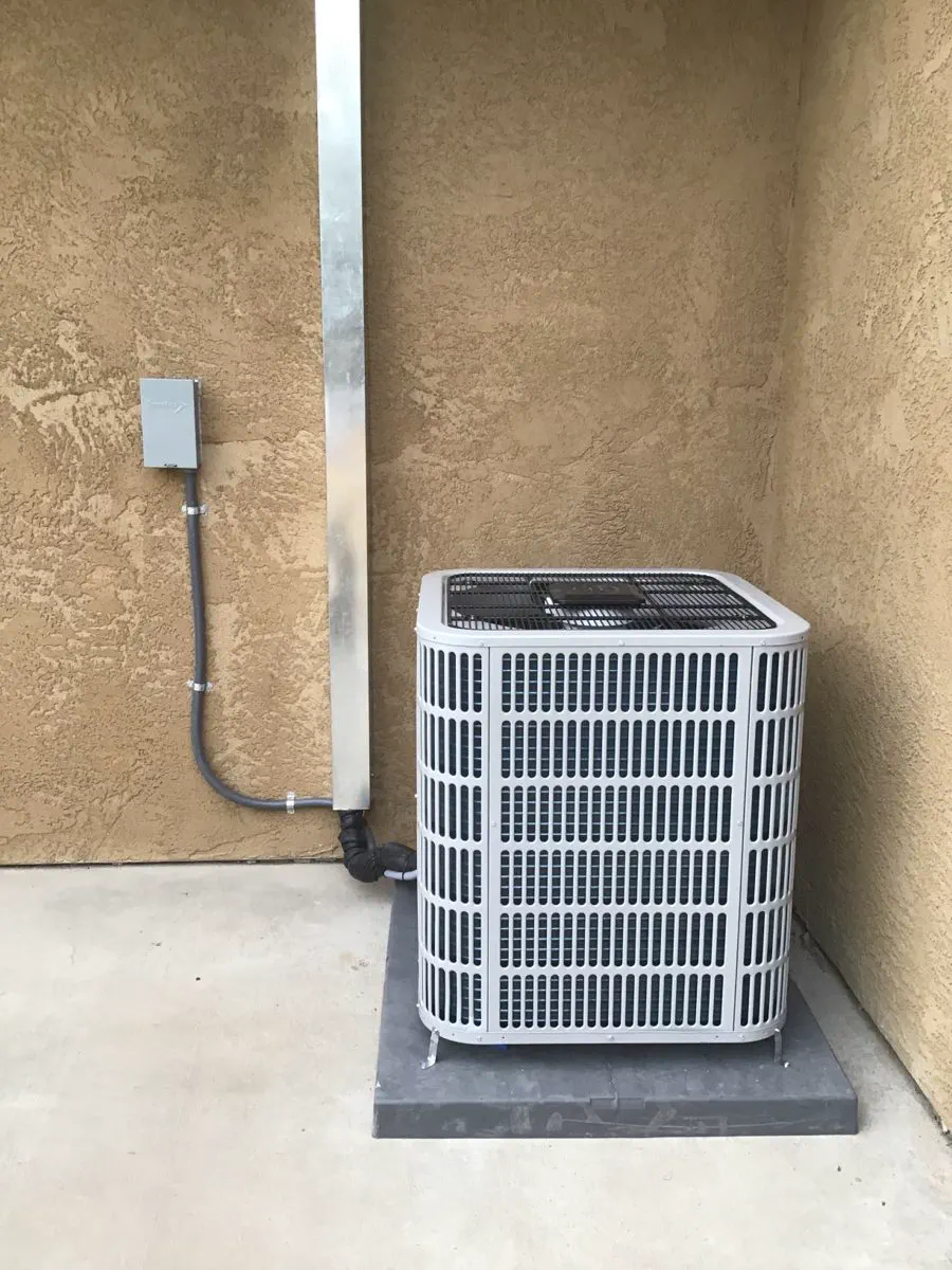 A white condenser unit installed on a pad at a stucco home