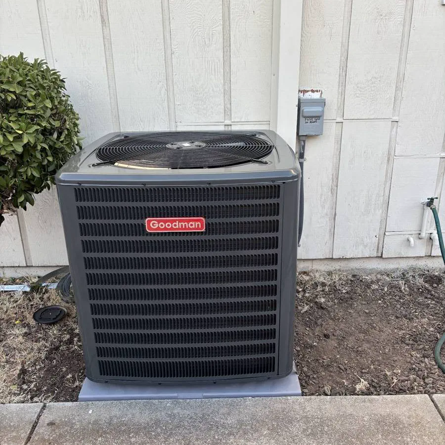 A new Goodman condenser on a fresh pad beside a house